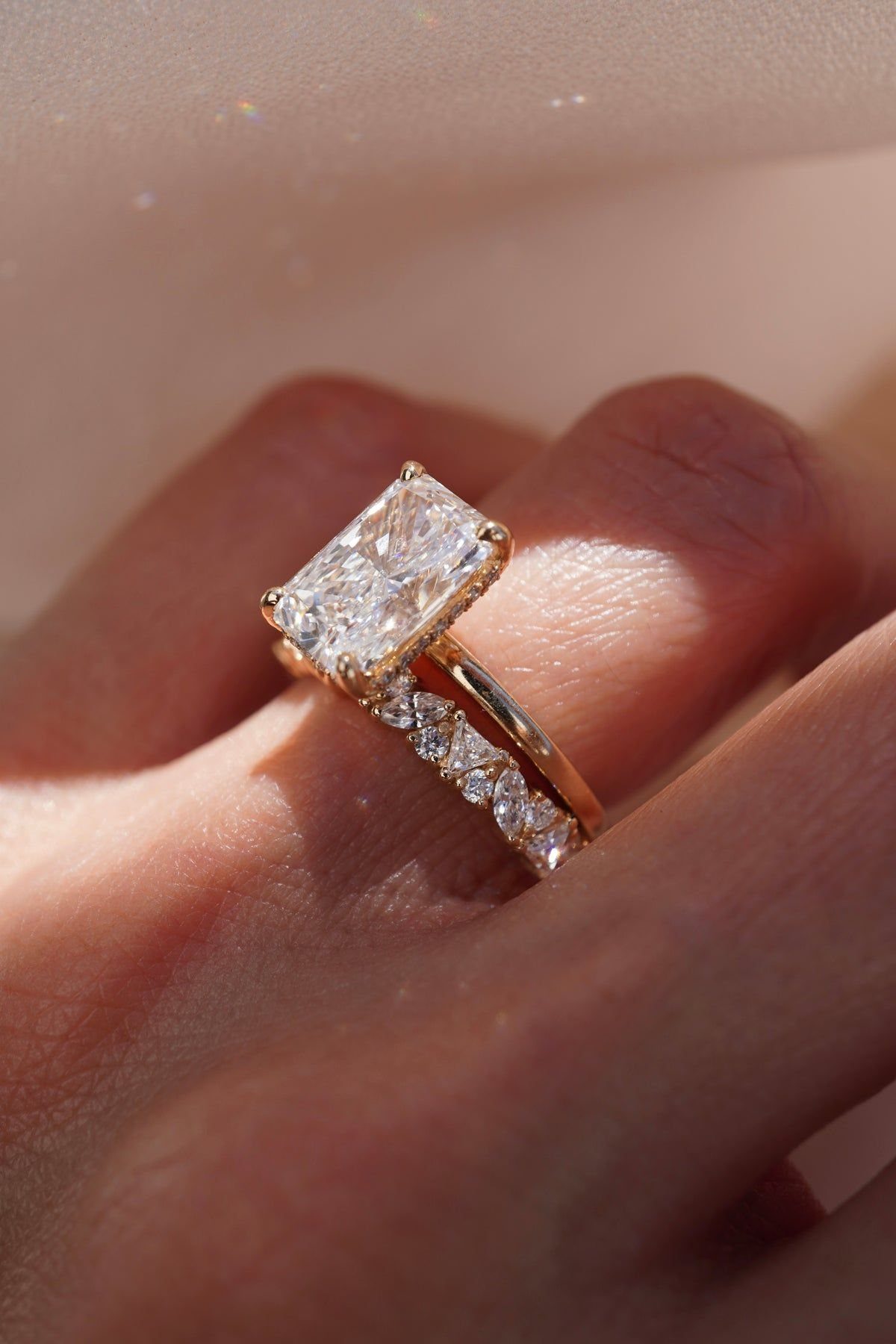 Gold rings with a large emerald-cut diamond and a diamond band on a finger