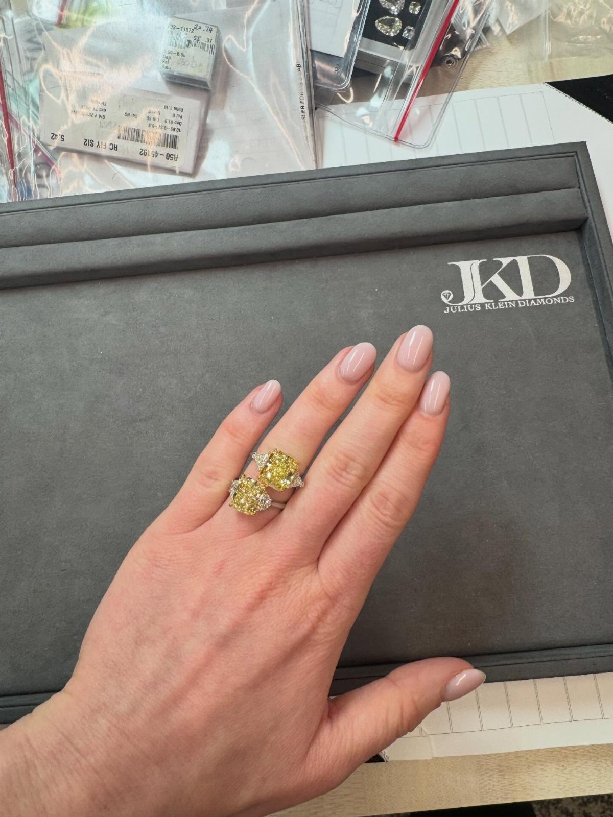 Two yellow diamond rings on a woman's finger resting on a grey box.