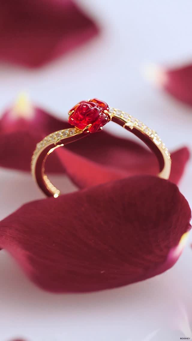 Gold ring with red rose gemstone resting on red rose petals
