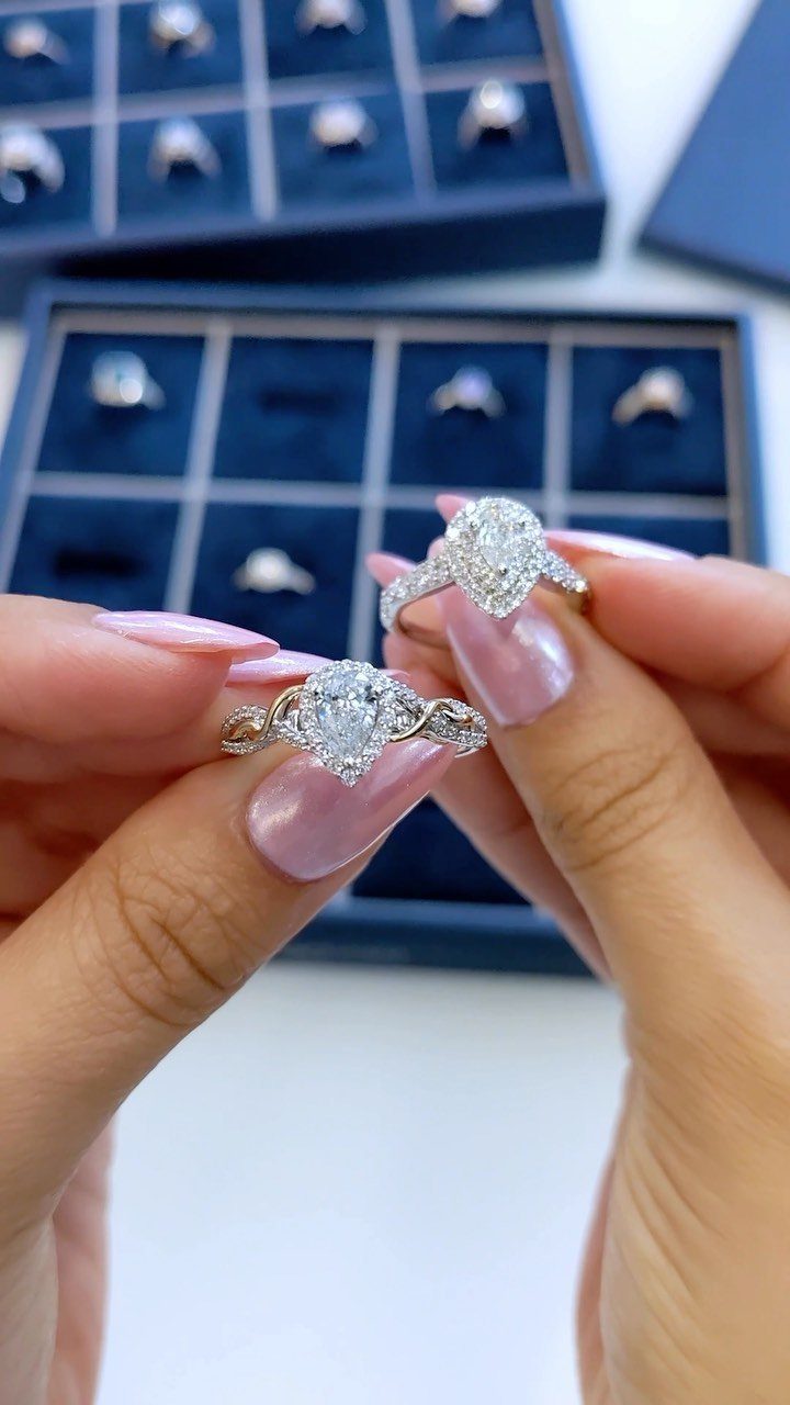 Two diamond engagement rings held by hands over blue velvet jewelry boxes.