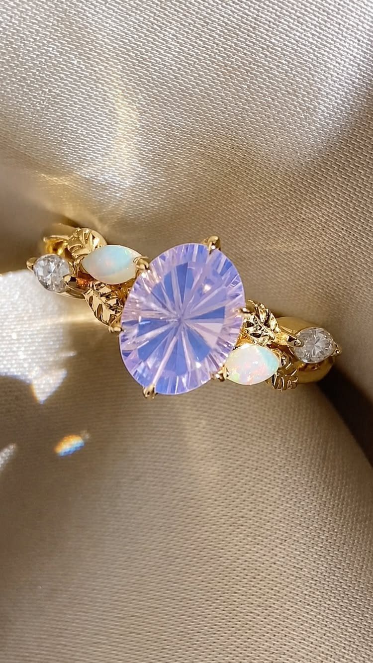 Gold ring with purple oval gemstone, opals, and diamonds on beige fabric.