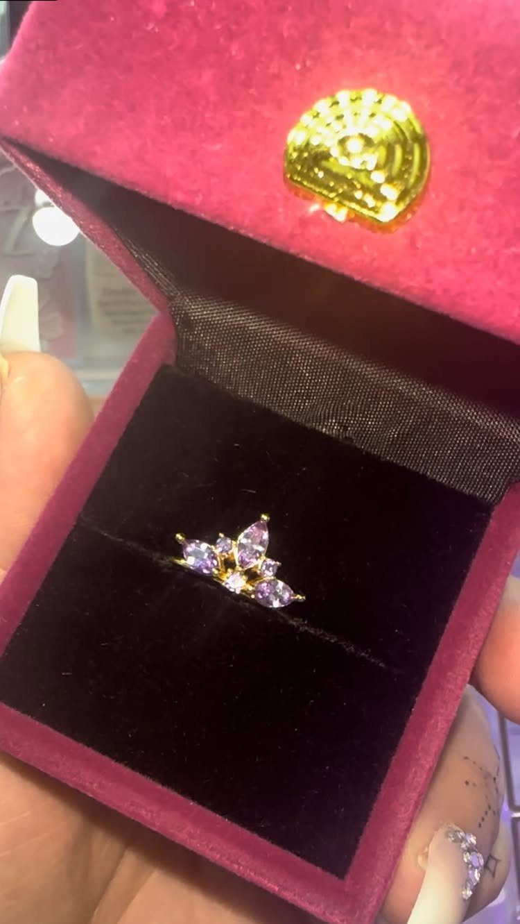 Gold ring with purple gemstones in a tiara shape inside a magenta box.