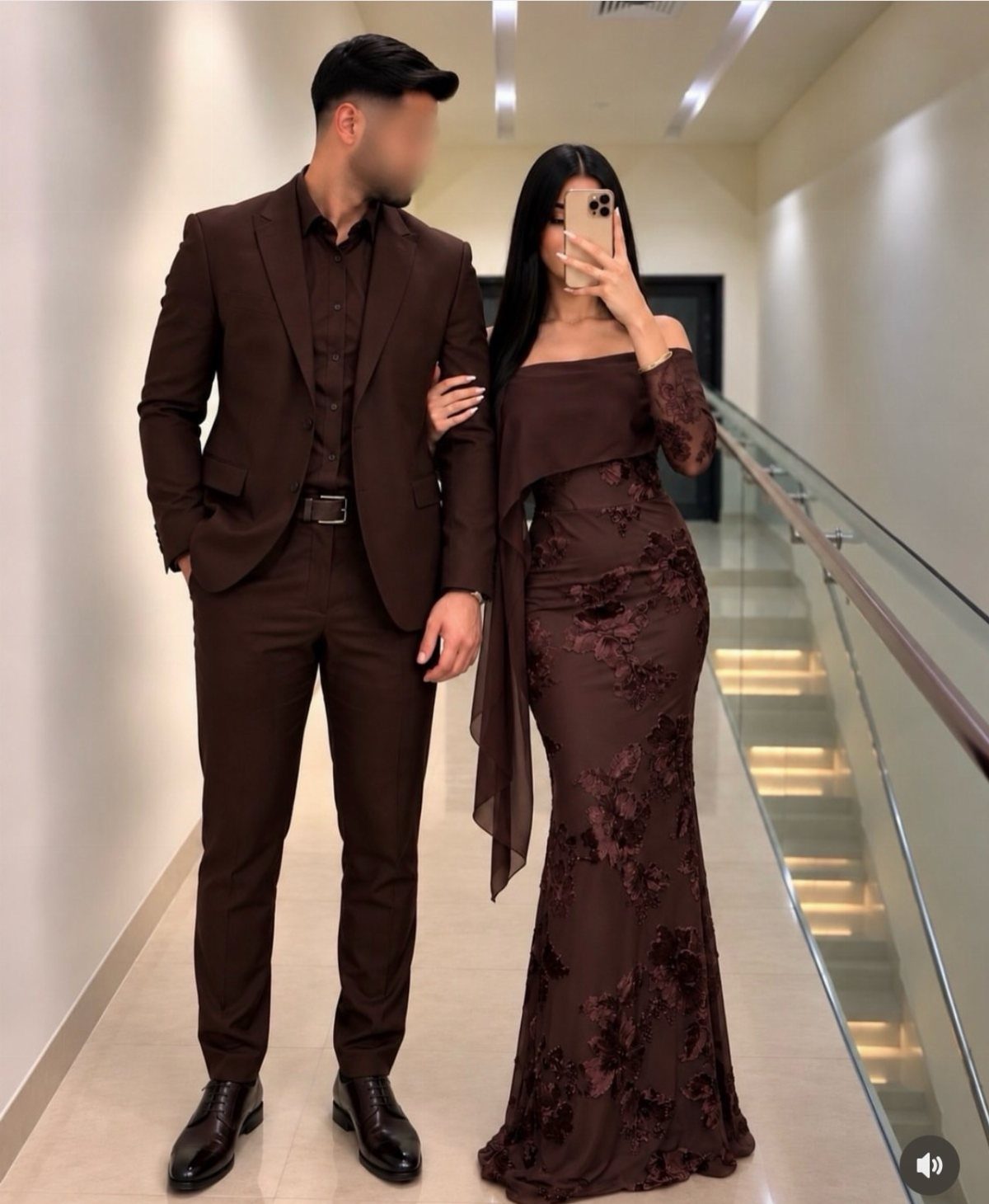Couple posing in matching dark brown formal attire in a modern hallway