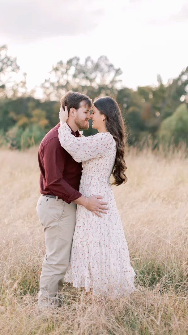 Couple embracing in a field, woman wearing a long flowy floral dress.