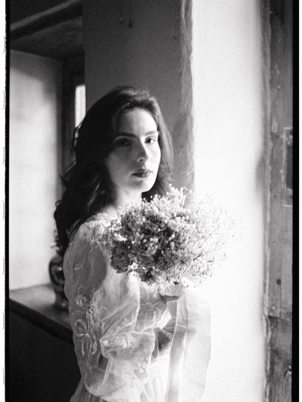 Woman in a lace dress holding a bouquet of small white flowers indoors.