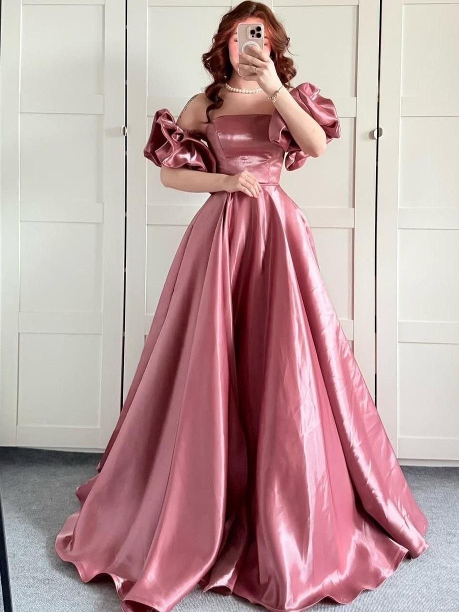 Woman in a shimmering rose-pink satin gown with puff sleeves taking a mirror selfie.