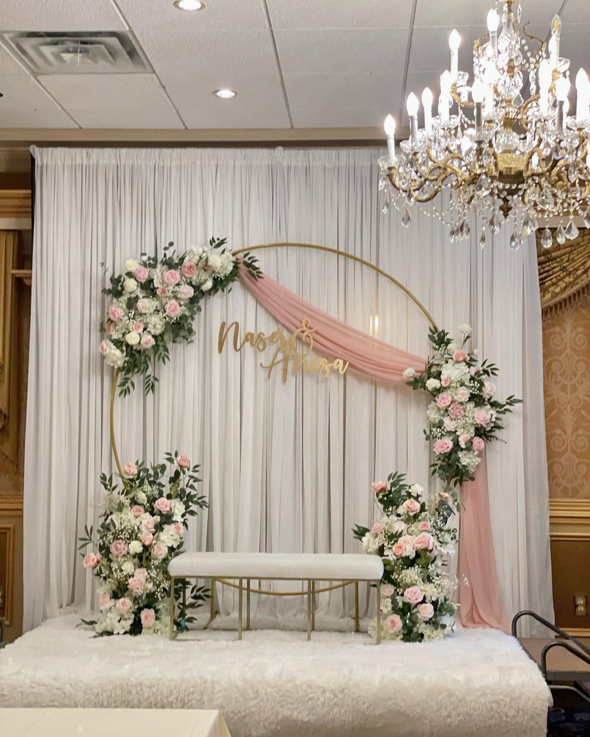 Gold circular backdrop with pink and white flowers, pink fabric, and white bench.