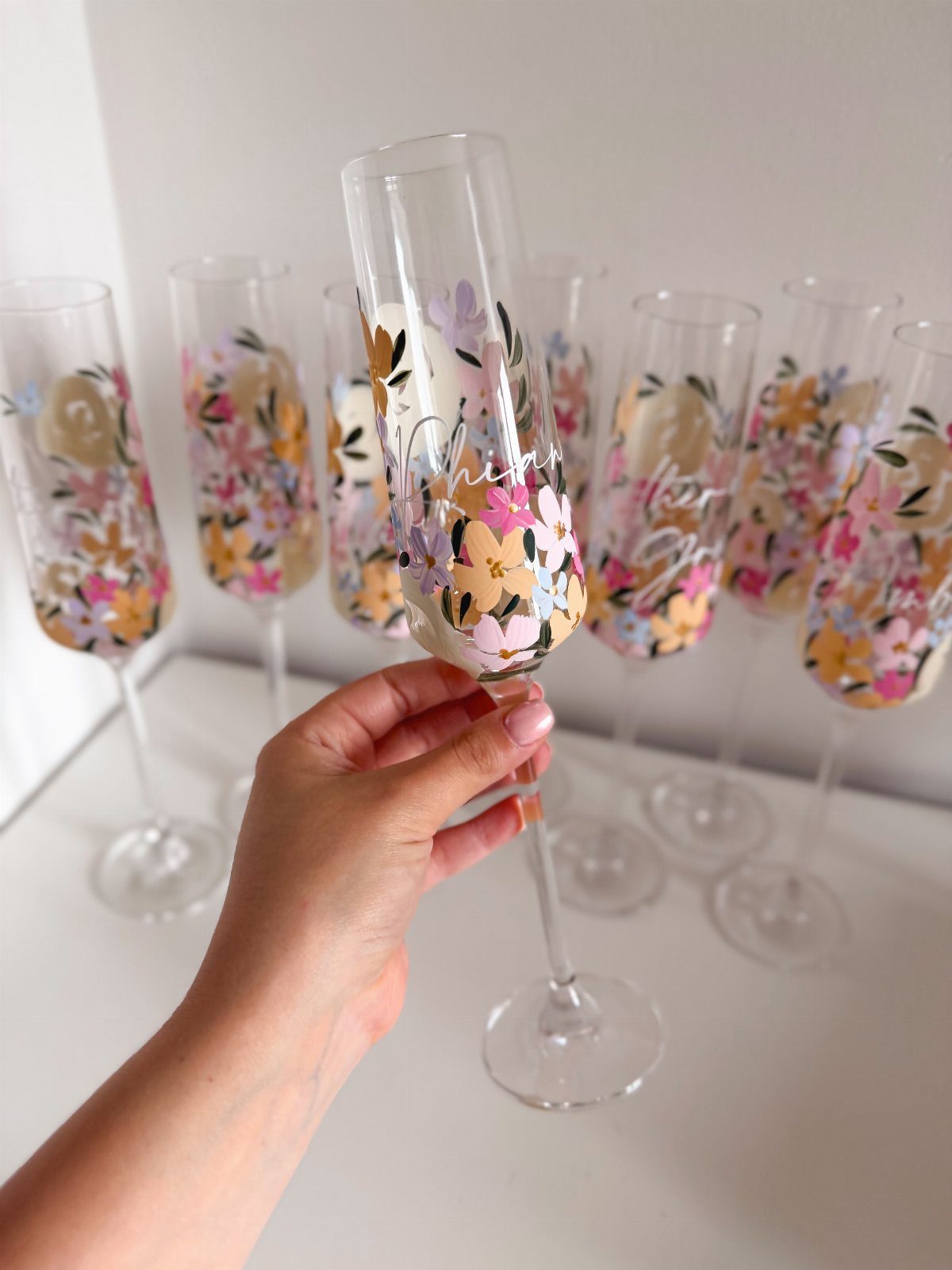 Champagne flutes with colorful floral designs and personalized cursive text on glass.