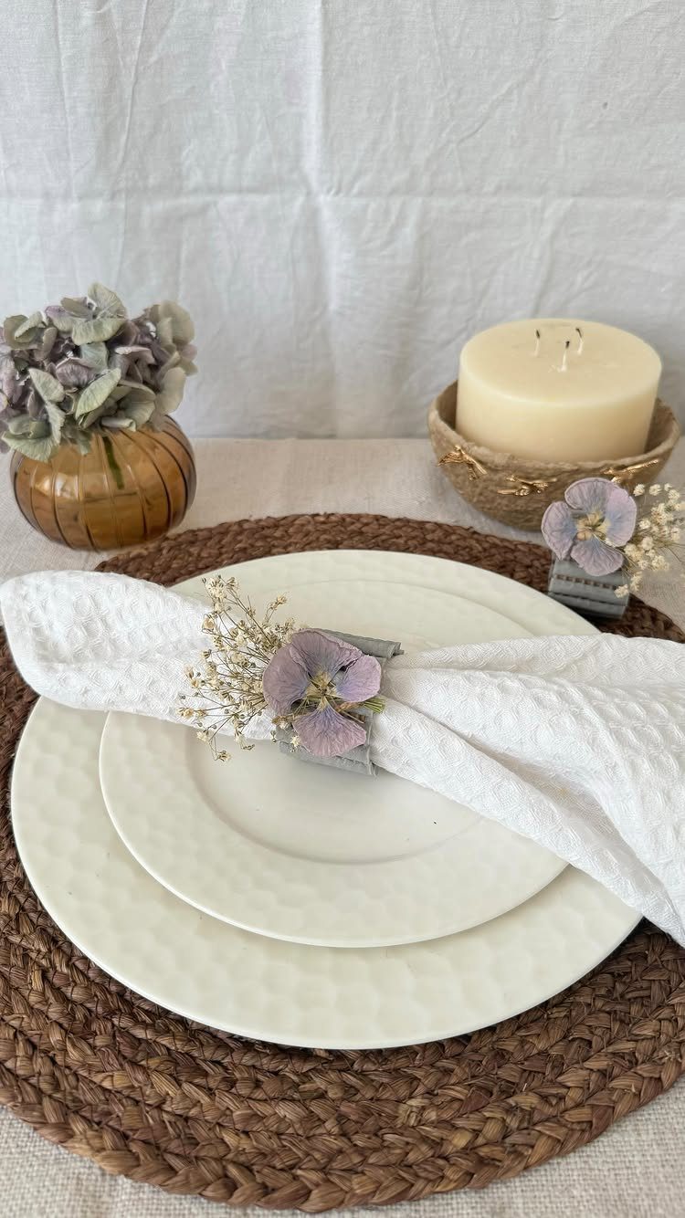 White napkin with dried purple flower ring on white plates and woven charger