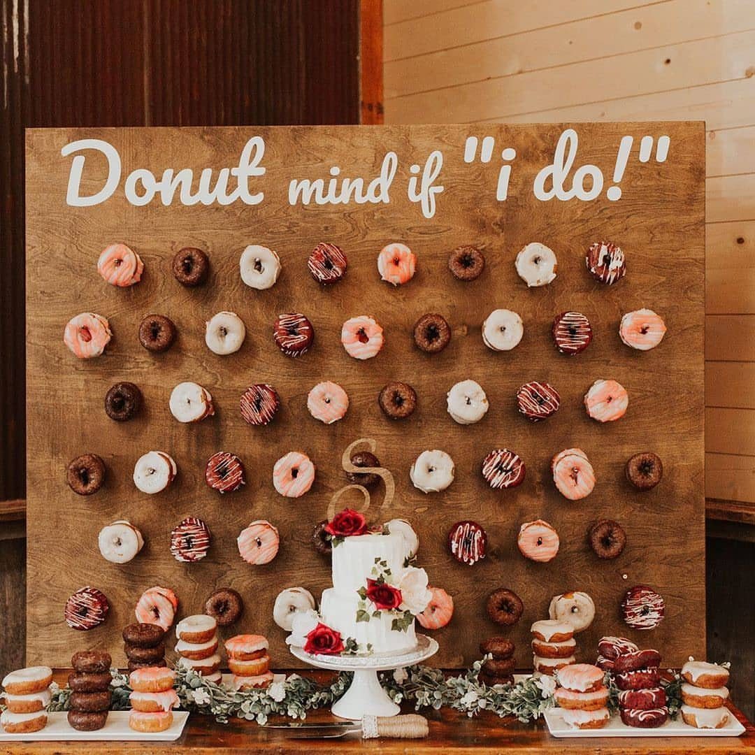 Wooden donut wall with assorted donuts and a small white wedding cake.
