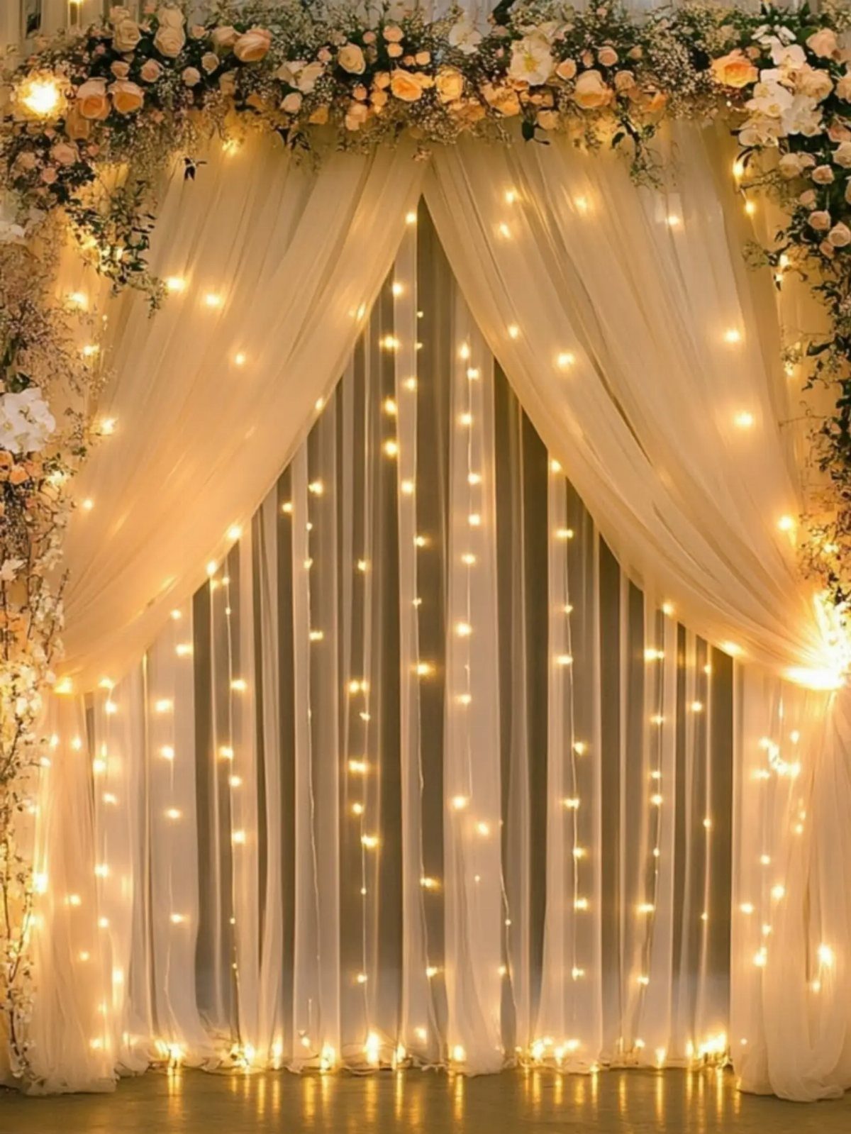 White sheer curtains with warm string lights topped with peach and white flowers