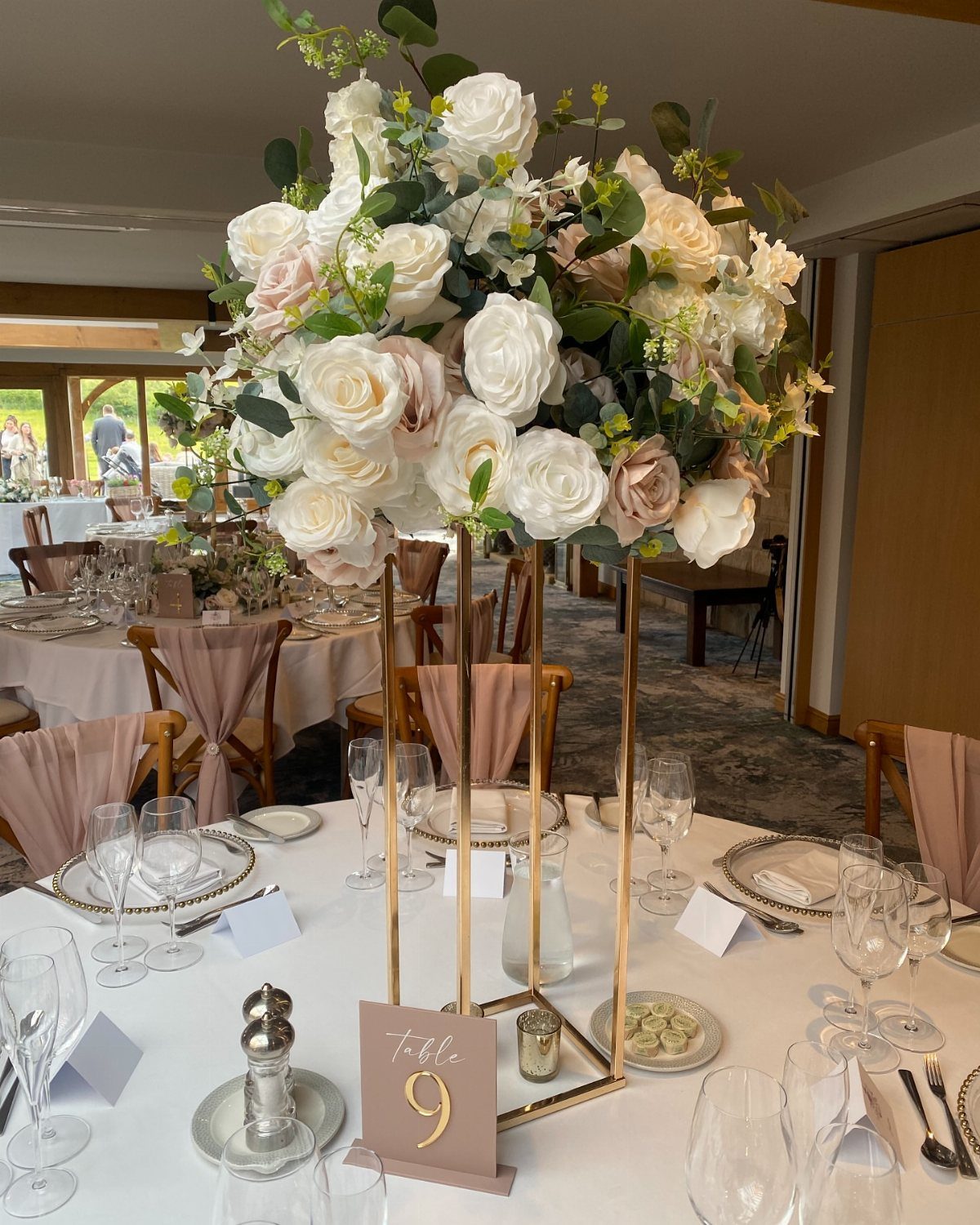 Tall gold stand with white and cream rose floral centerpiece on a banquet table.