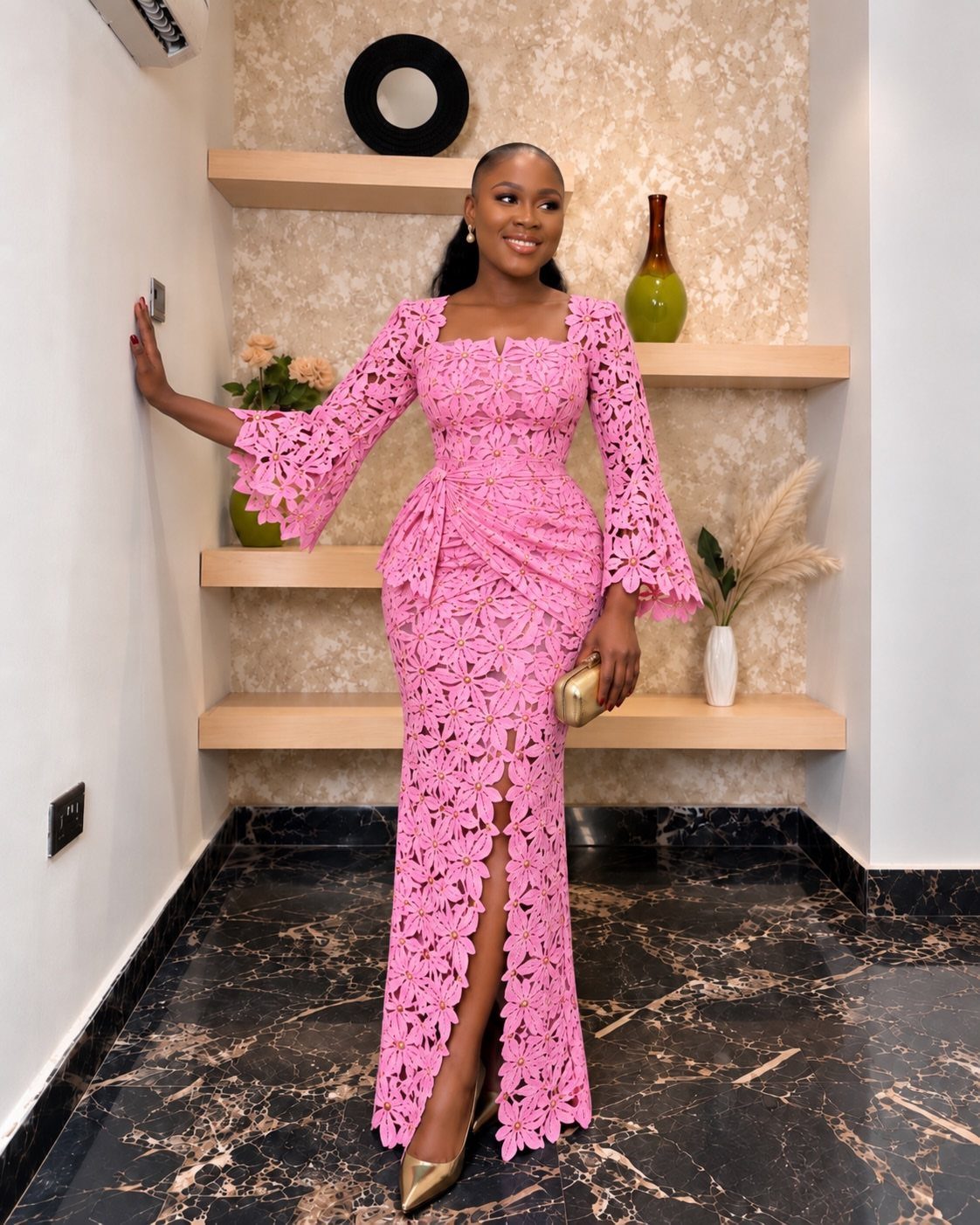 Woman in a long pink lace dress with bell sleeves and gold clutch.