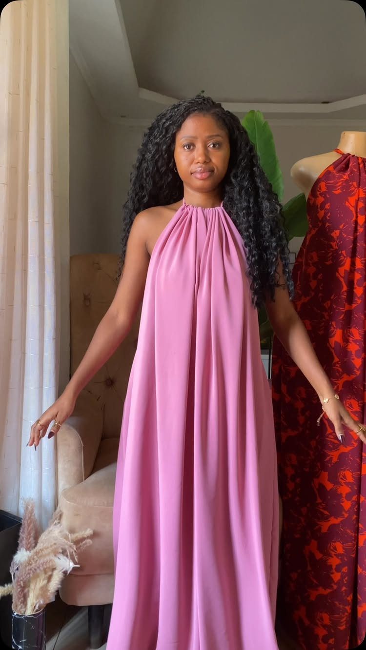 Woman wearing a long sleeveless pink halter-neck maxi dress standing indoors.