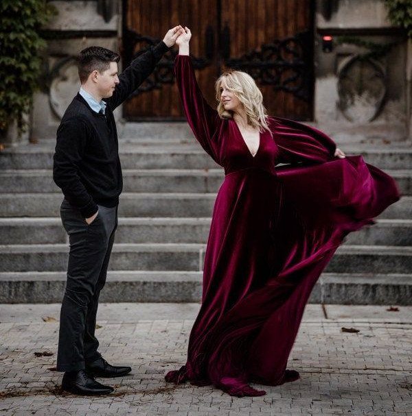 Woman in burgundy velvet gown dancing with man in black attire outdoors