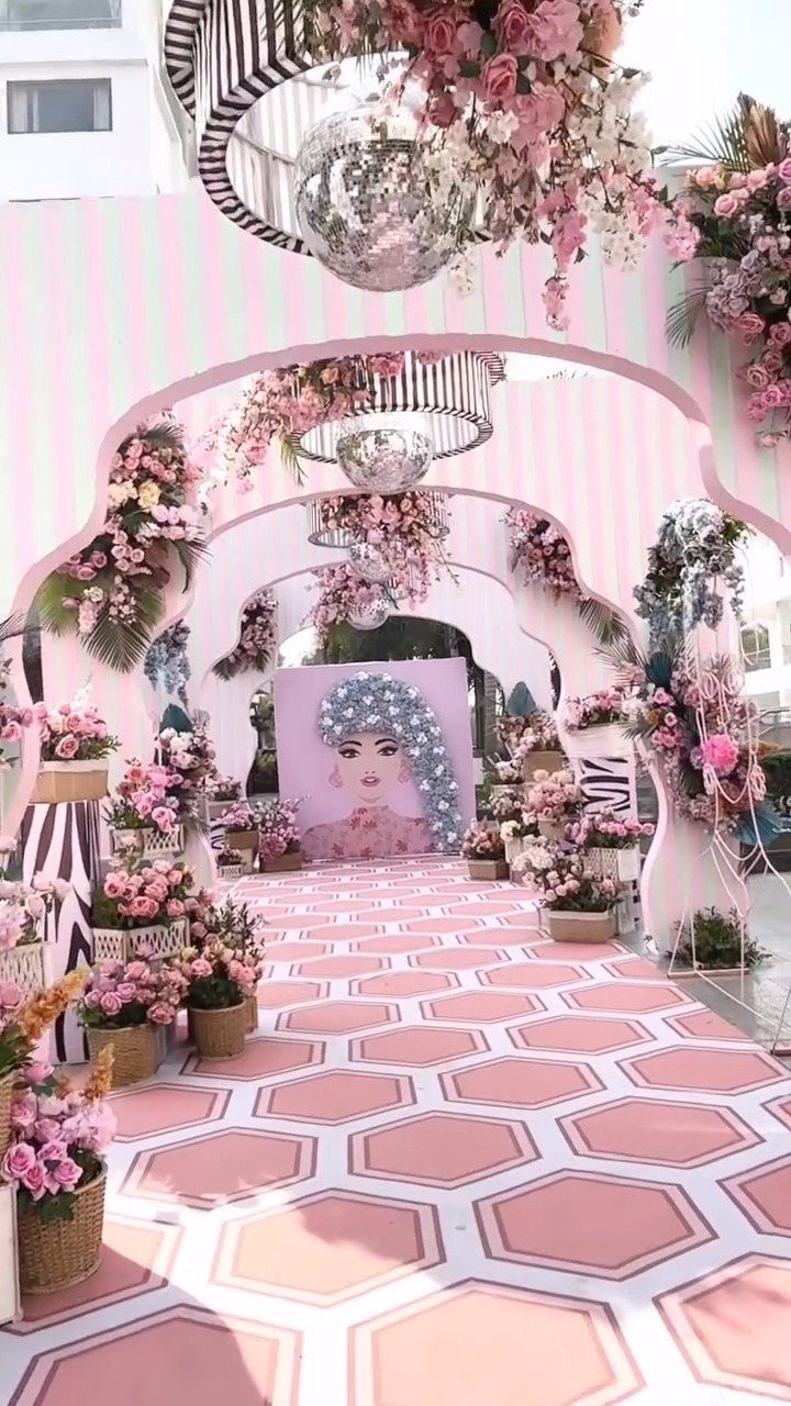 Pink and white striped event decor with floral arches and hexagonal patterned flooring.