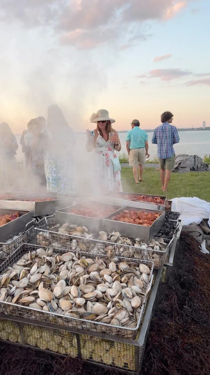 Steaming trays of clams and lobster at an outdoor seaside seafood feast.