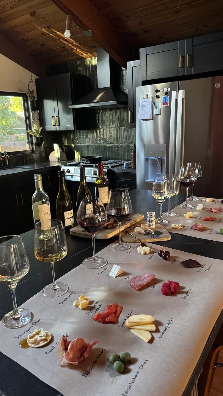 Wine tasting spread with glasses, bottles, and labeled charcuterie on a kitchen counter.