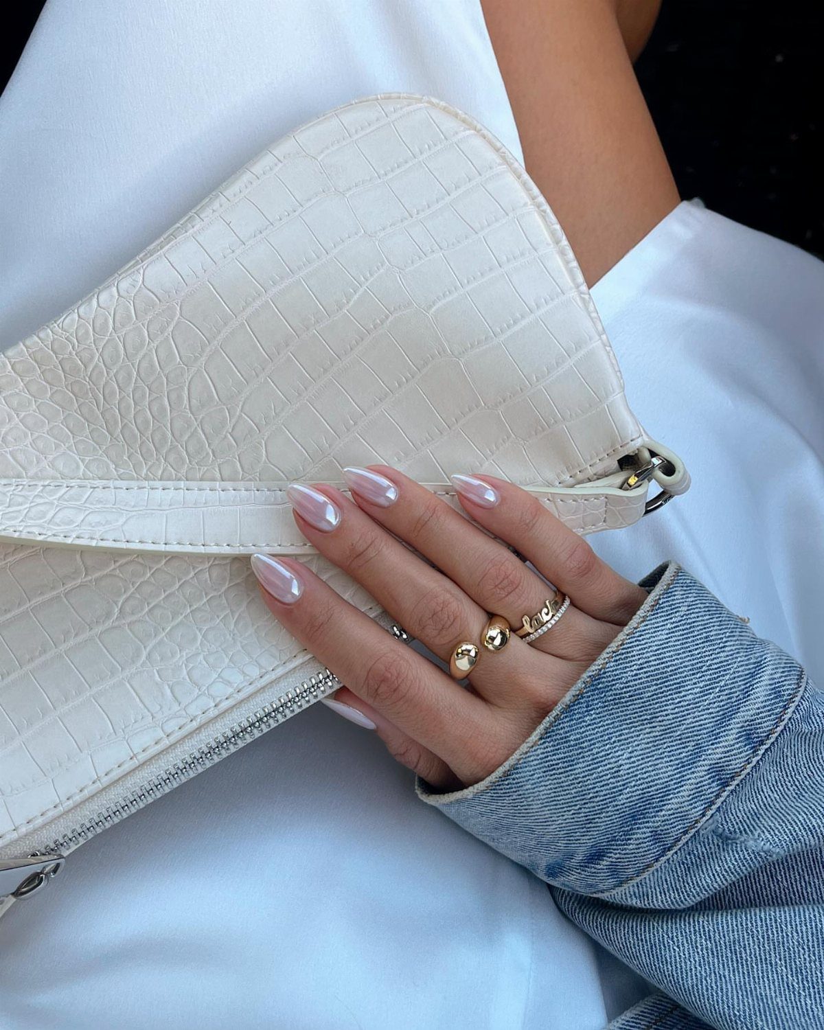 Pearlescent chrome nails on a hand holding a white croc-embossed leather handbag.