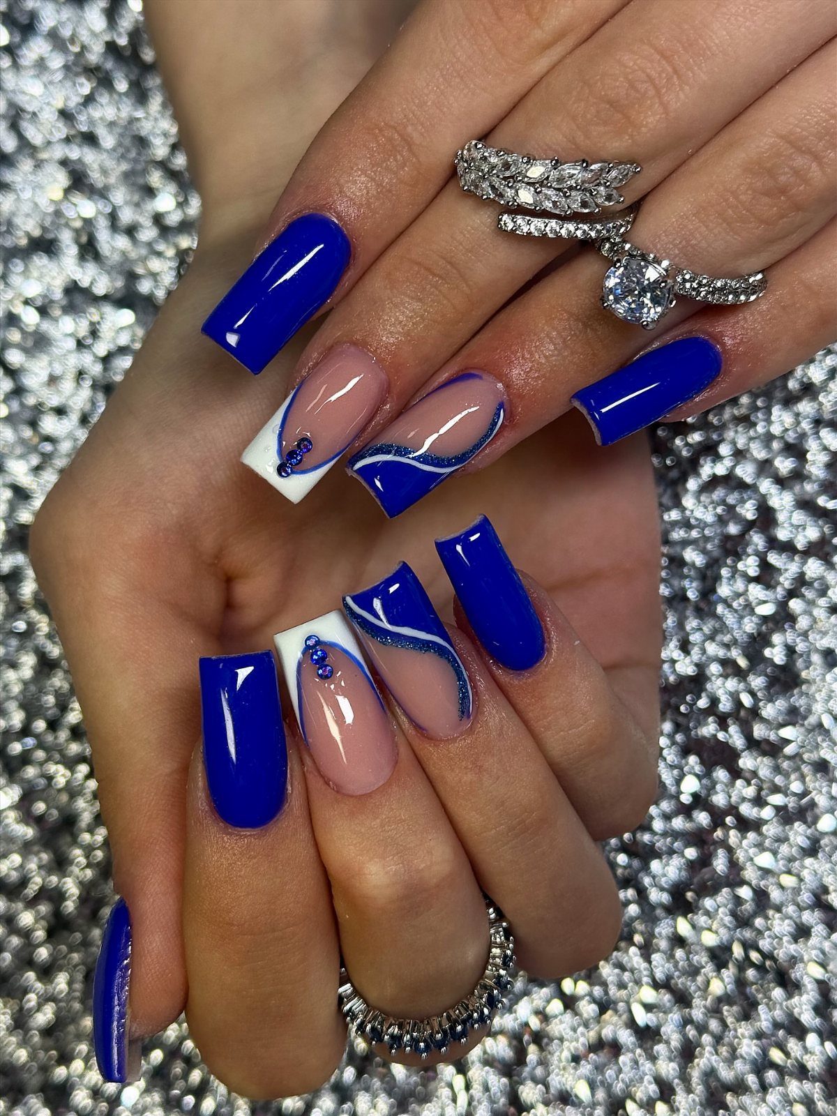 Deep blue and white swirling nail art on long coffin nails with diamond rings.