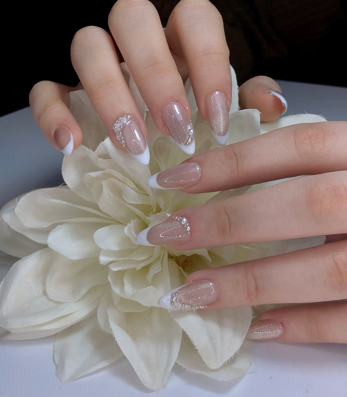 Almond shaped nails with white French tips and glitter resting on a white flower