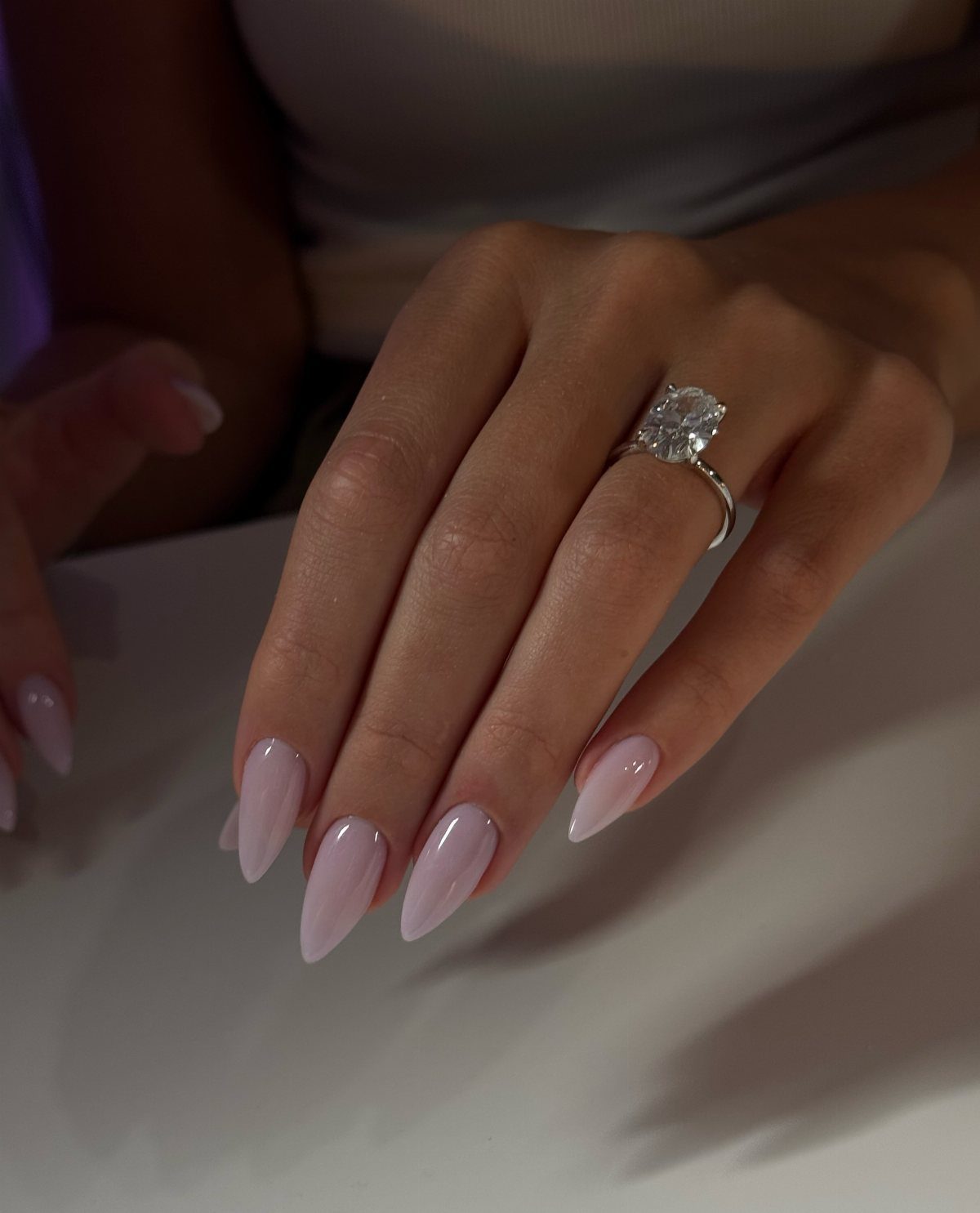 Pale pink almond-shaped nails with a large diamond engagement ring on finger