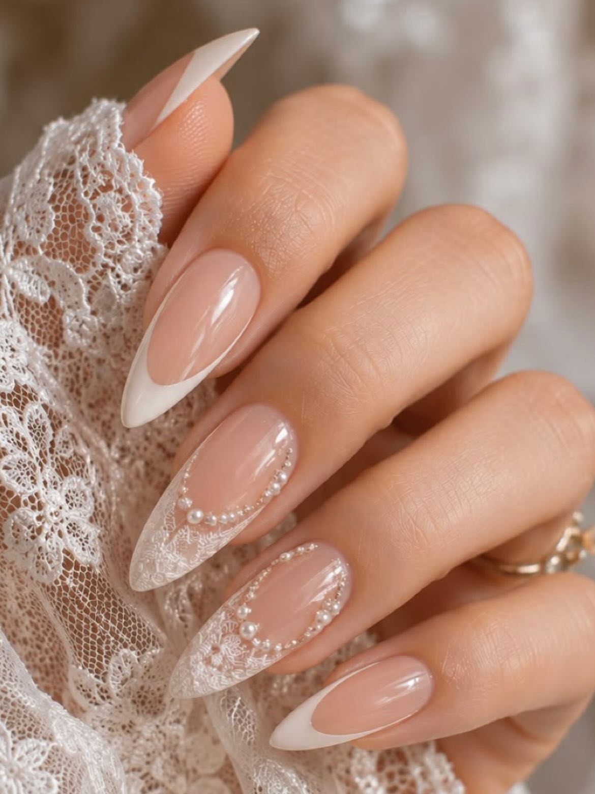 Almond nails with white French tips and pearl accents against white lace fabric