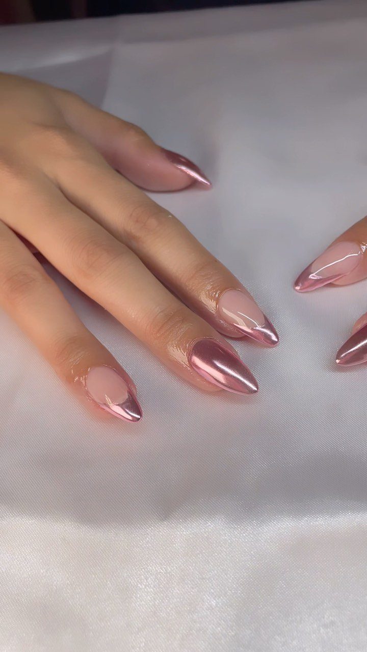 Almond-shaped nails with metallic rose gold chrome finish on white satin fabric.