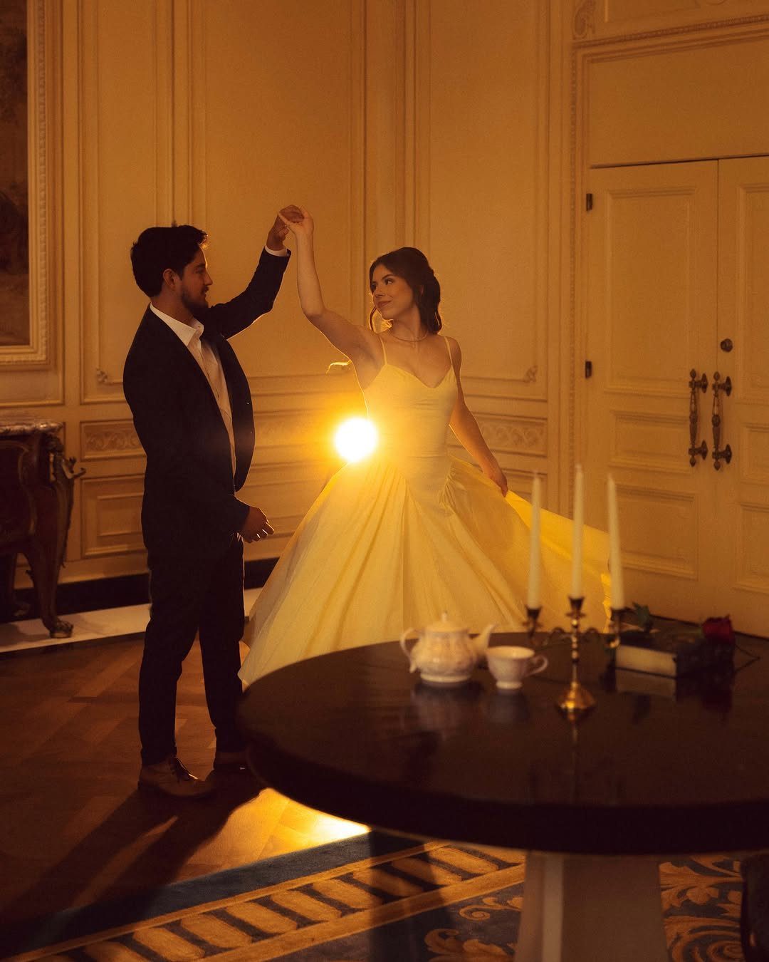Couple dancing in a grand room, woman wearing a large yellow ballgown.