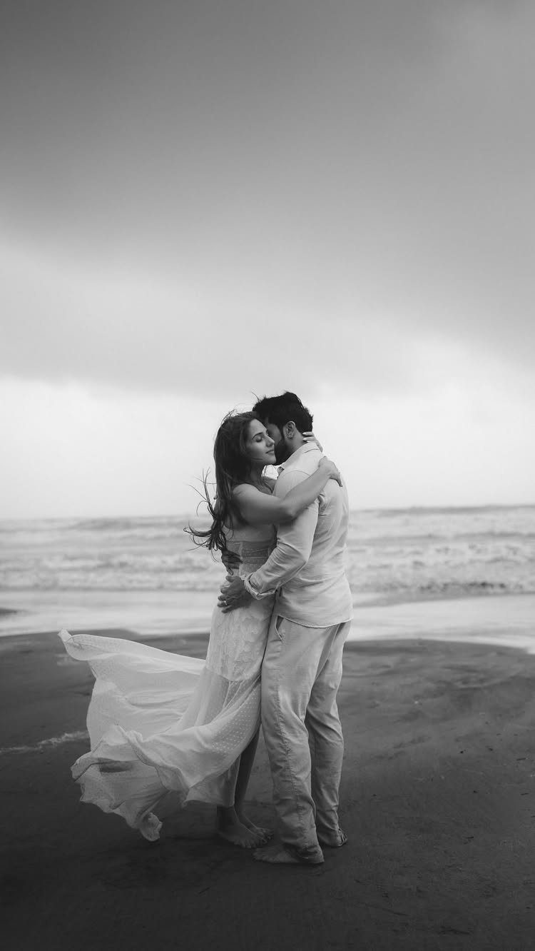 Couple embracing on a sandy beach with a flowing white dress blowing in wind.