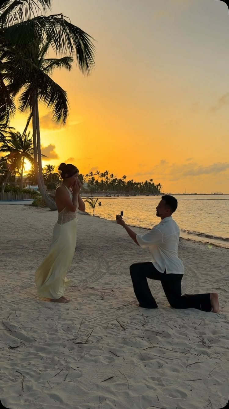 Man kneeling on a beach proposing to a woman during a golden sunset.