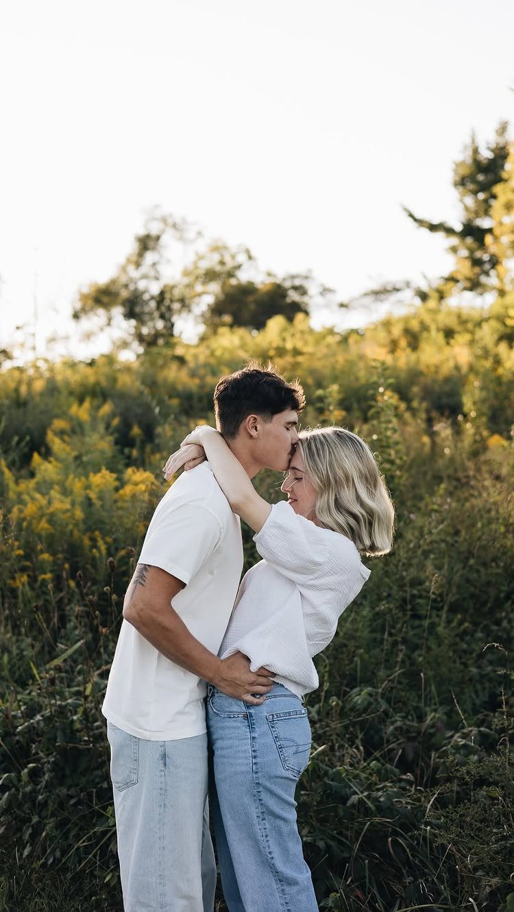 Couple embracing in a wildflower field with the man kissing the woman's forehead.