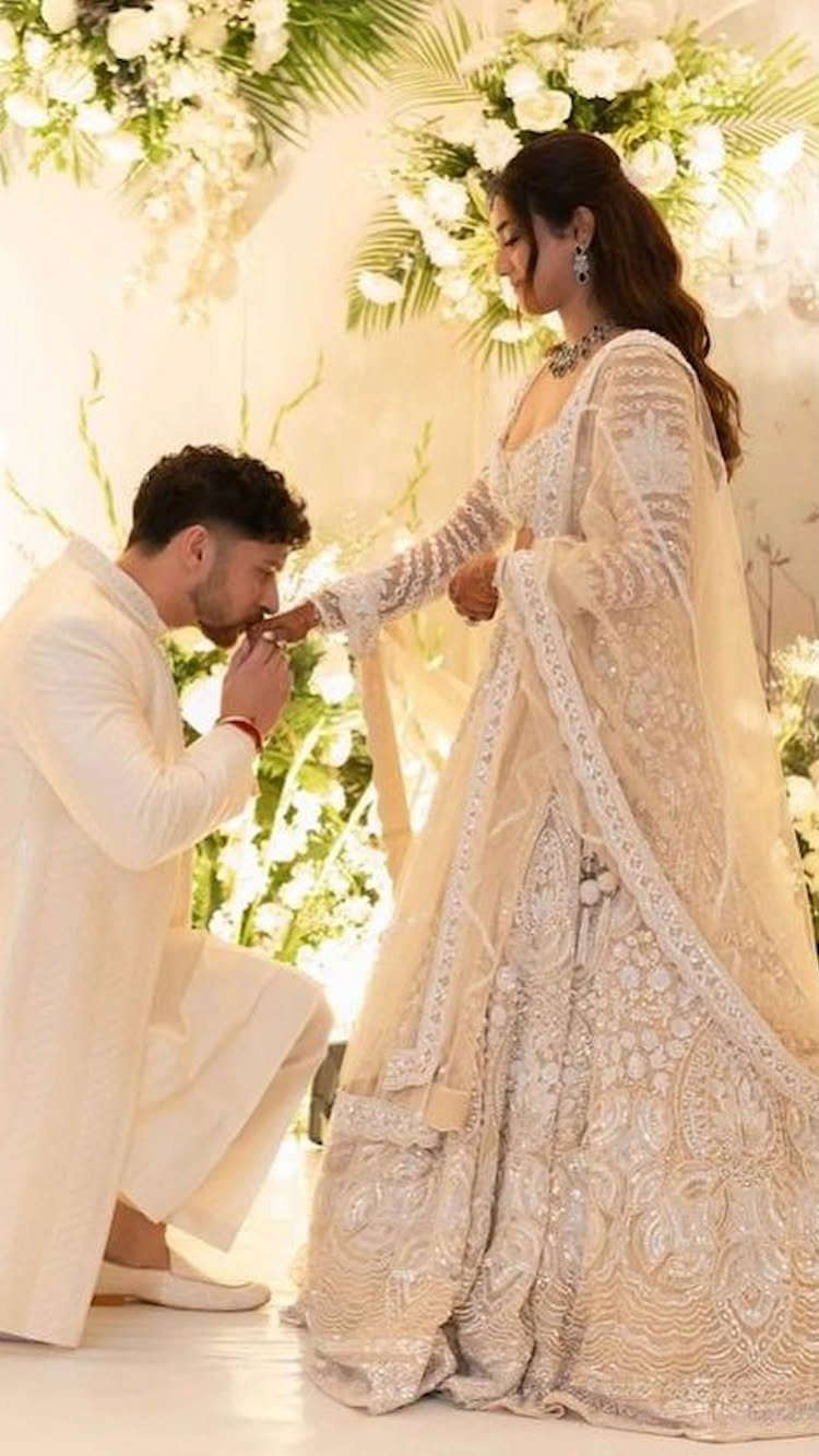Man kneeling and kissing the hand of a woman in traditional Indian attire.