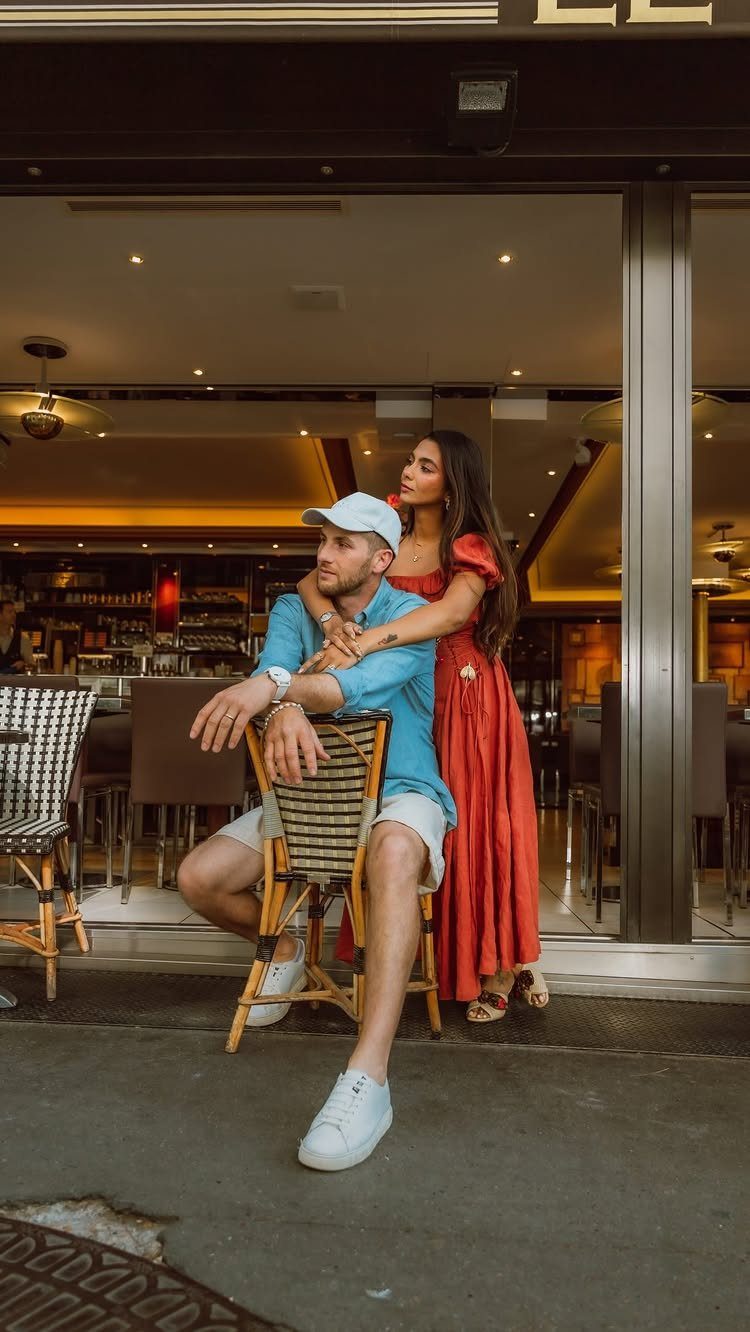 Man sitting on a chair while a woman in a red dress hugs him from behind.