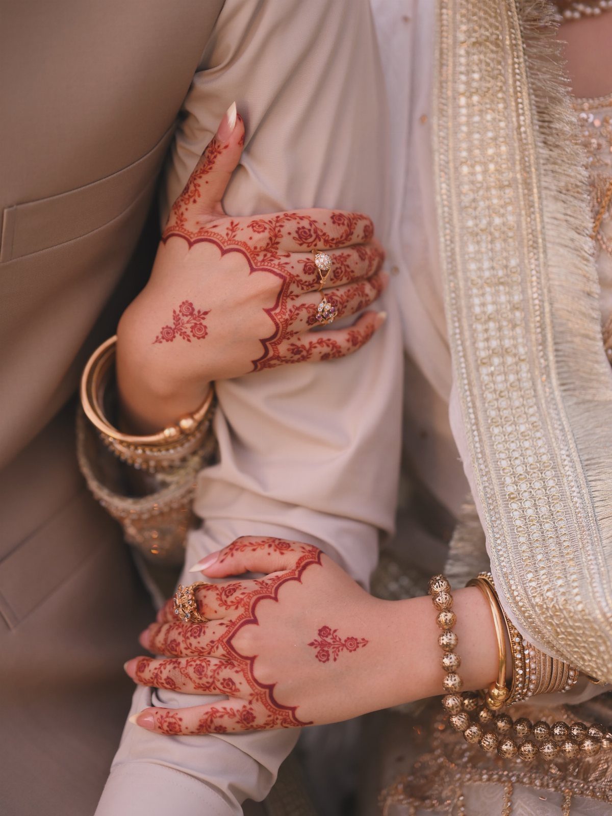 Henna decorated hands of a woman resting on a man in beige suit