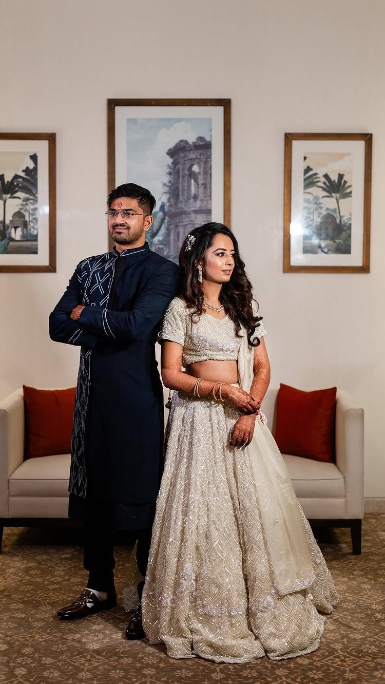 Couple in traditional Indian wedding attire standing side by side in a living room.
