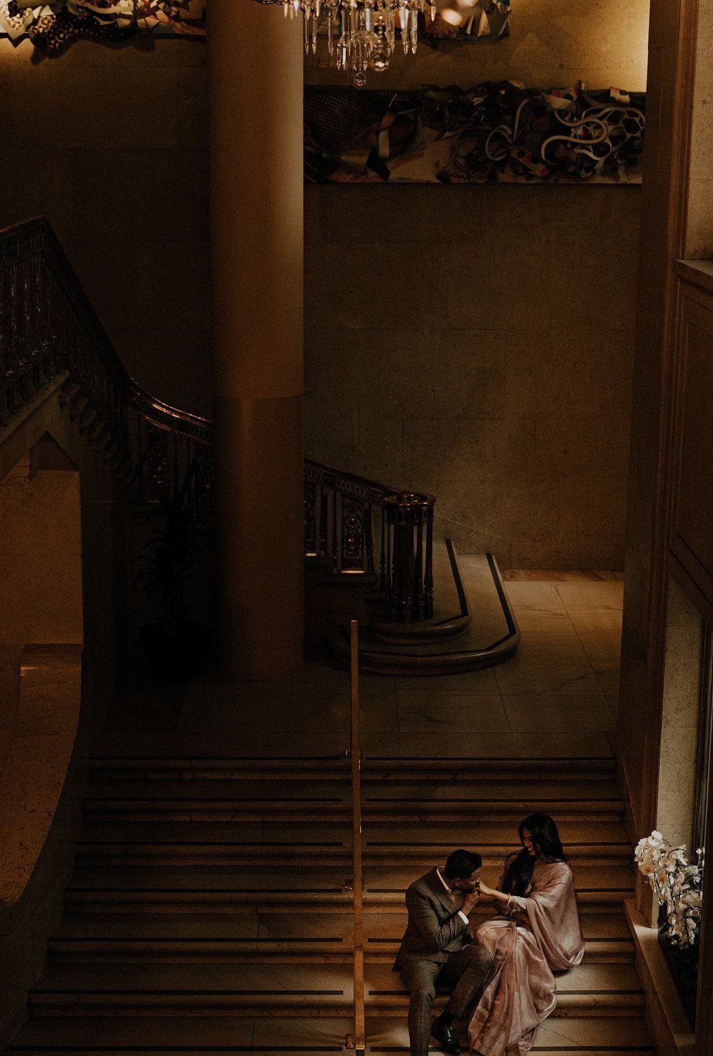 Couple in formal attire sitting together on a grand stone staircase in dim lighting.
