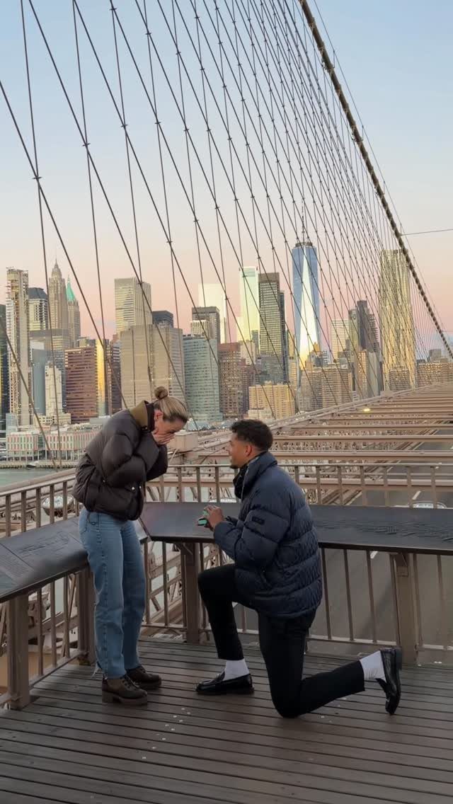 Man proposing to a woman on the Brooklyn Bridge with Manhattan skyline background