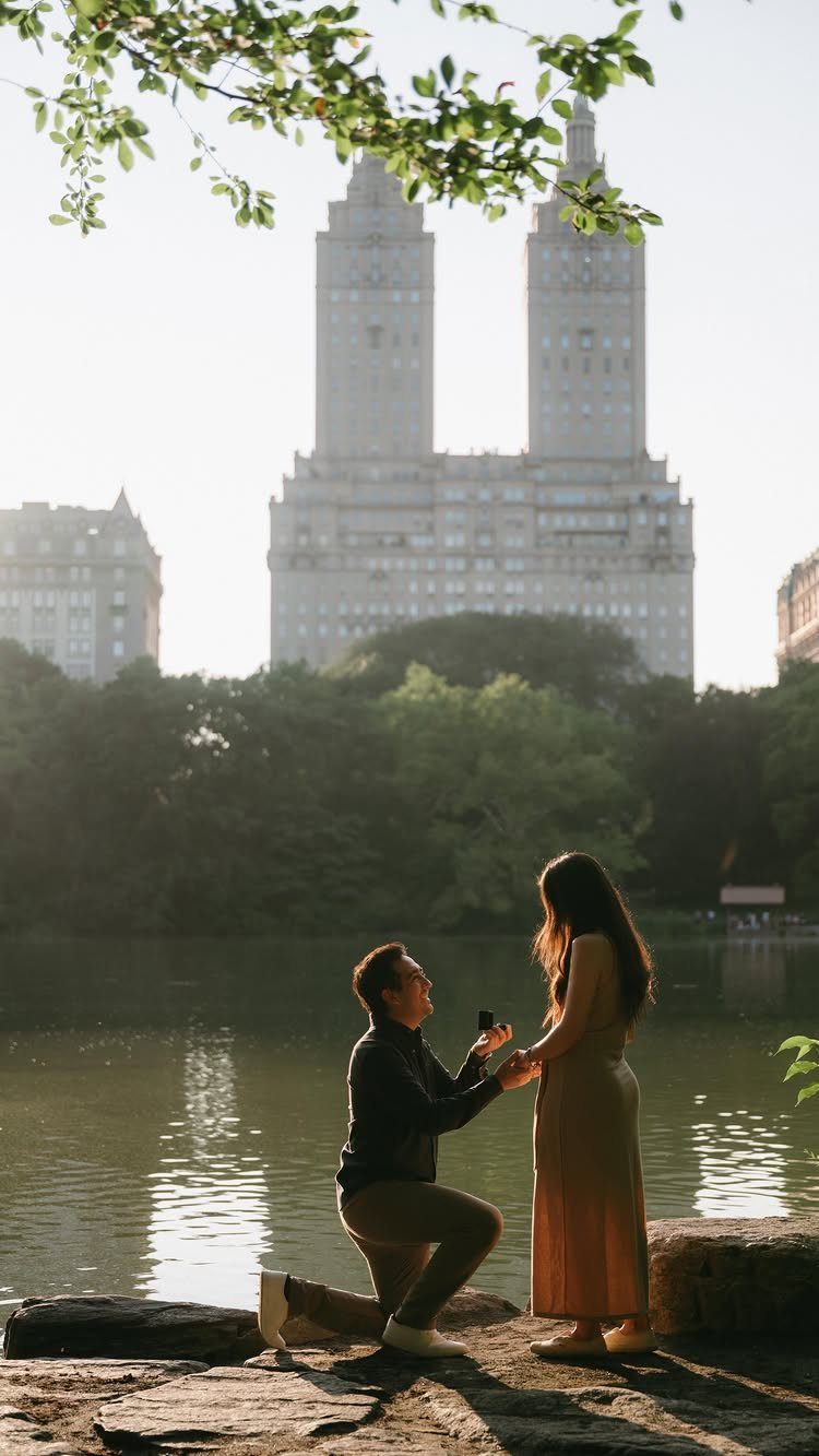 Man proposing to a woman by a lake with city buildings in background