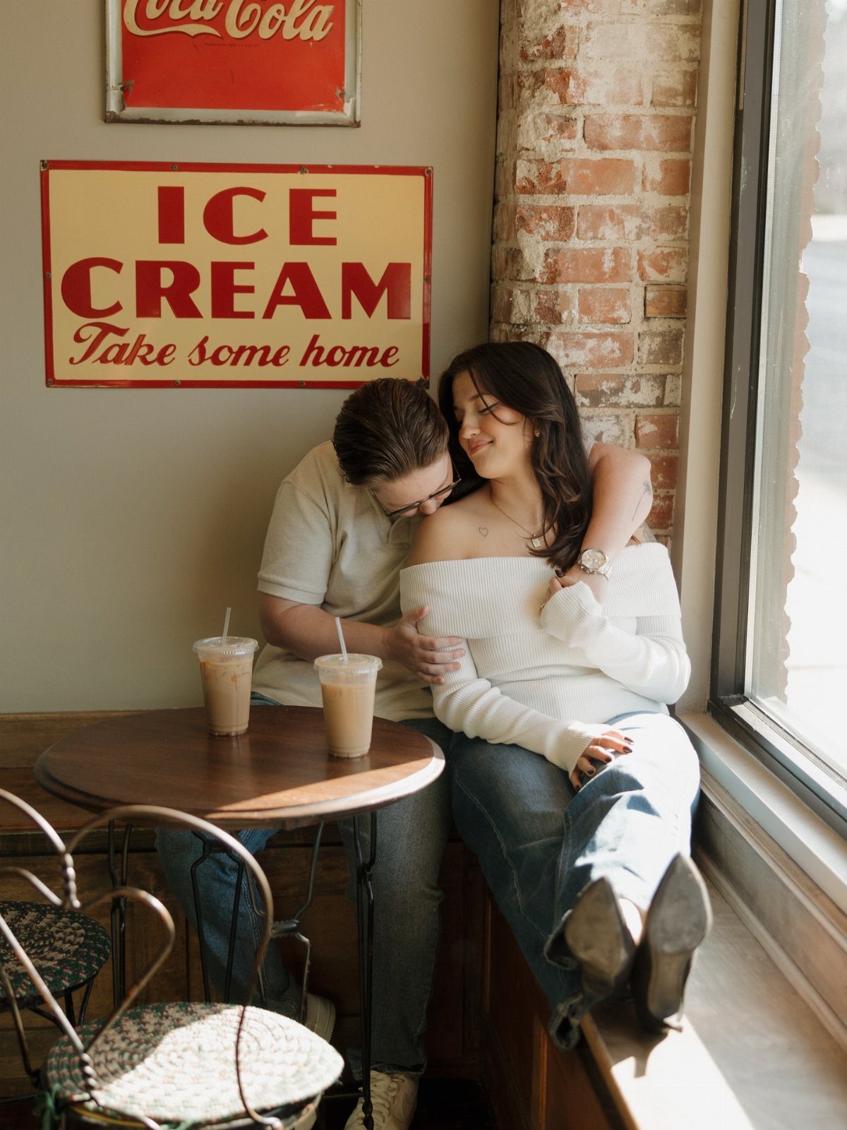 Couple embracing in a cozy cafe with vintage signs and iced coffees.