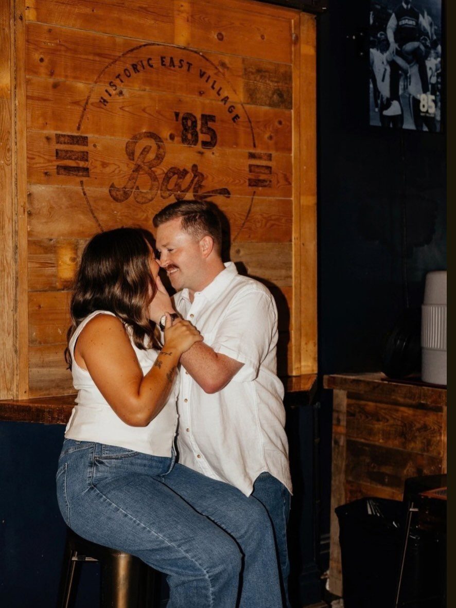 Couple embracing in a bar with a wooden wall reading Historic East Village