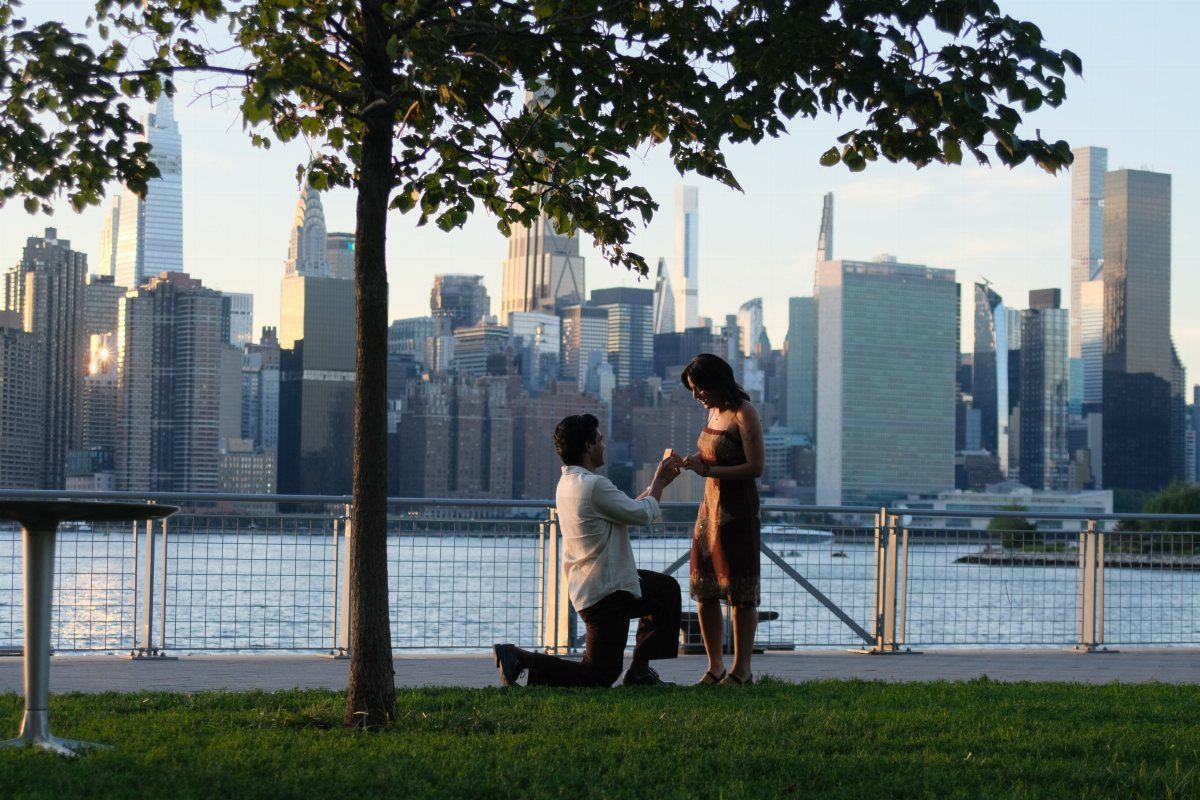 Man proposing to a woman in a waterfront park with Manhattan skyline background