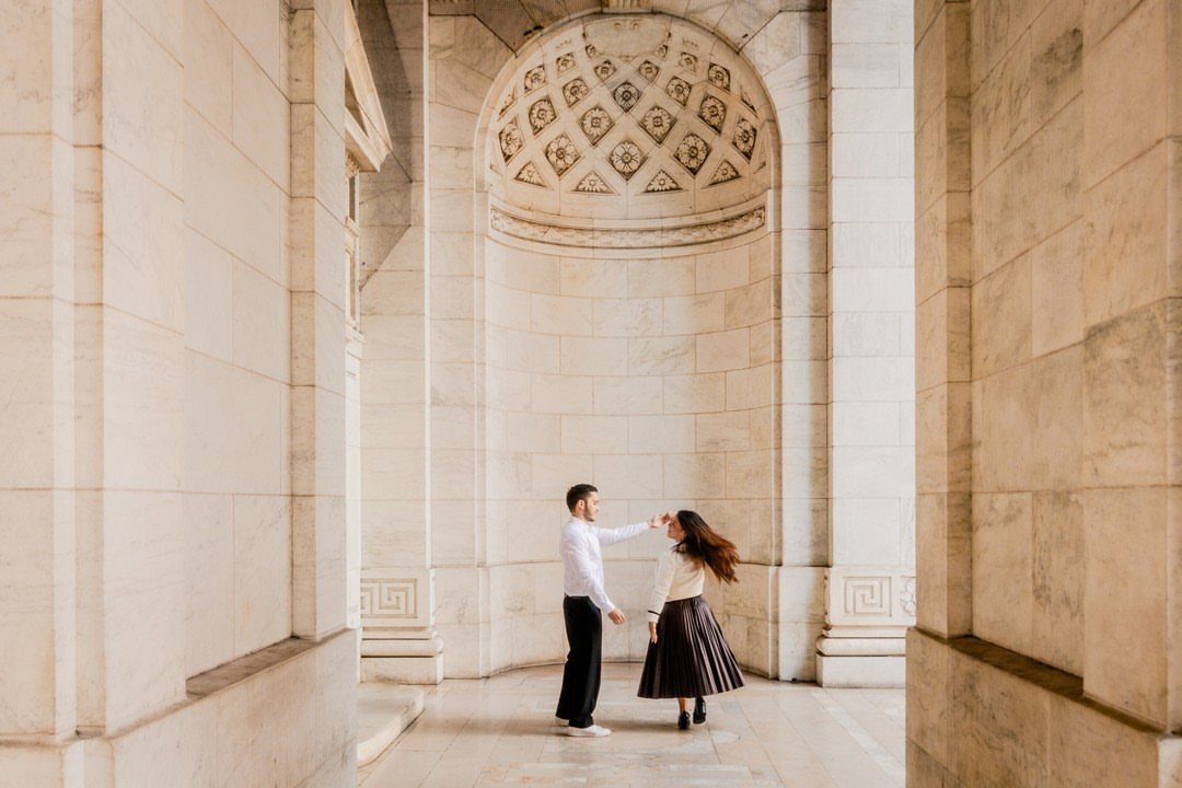 Couple dancing in a grand marble corridor with a decorative arched alcove.
