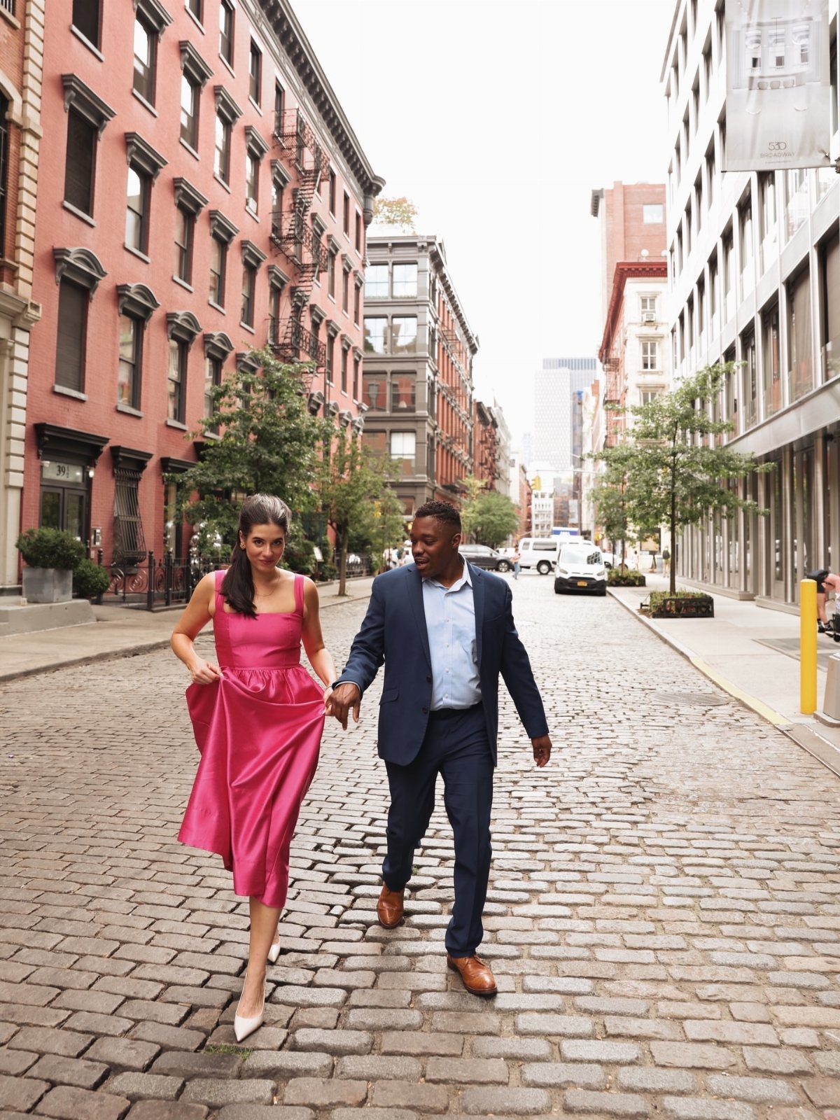 Couple in formal attire walking hand-in-hand down a cobblestone street in SoHo.