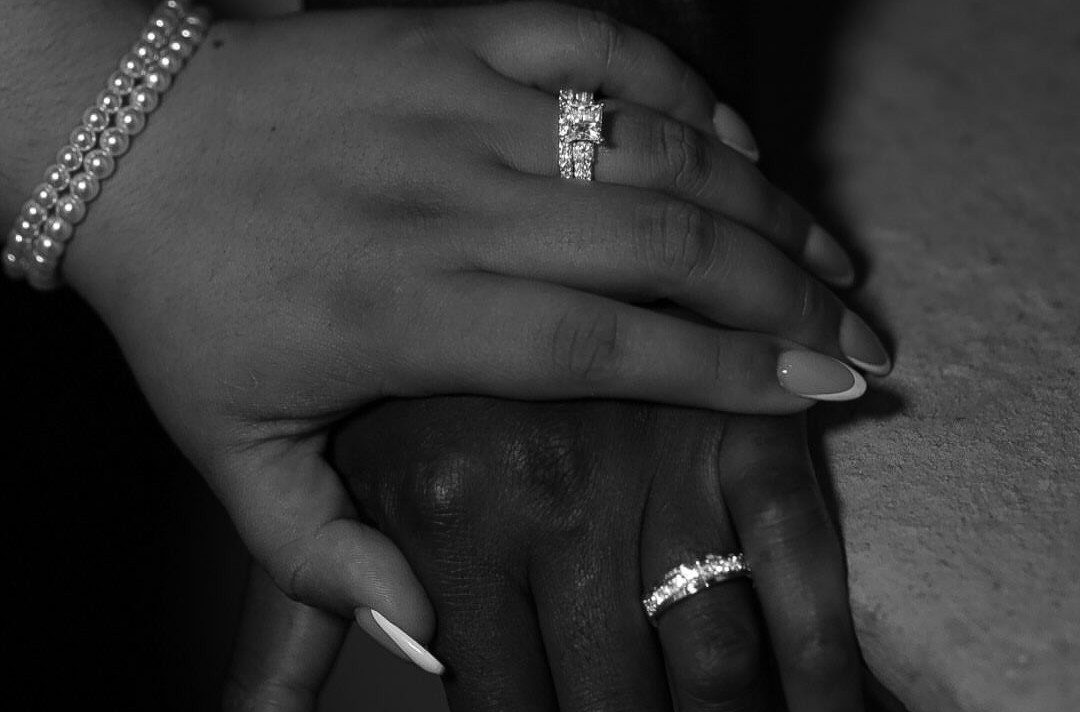 Two hands stacked wearing diamond rings in a black and white close-up shot.