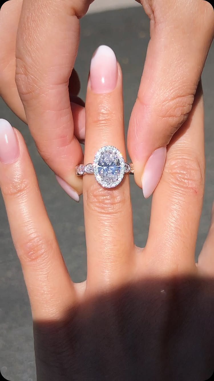 Oval diamond engagement ring on a finger with pink ombre manicured nails.