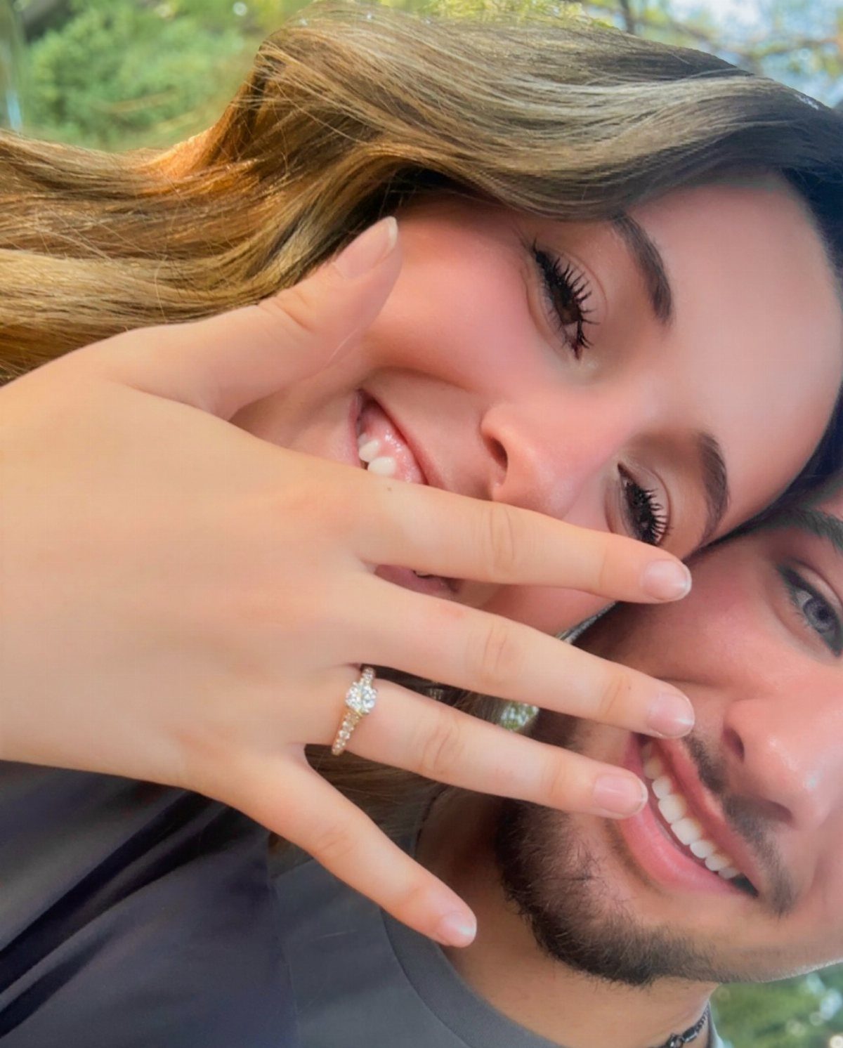 Smiling couple with woman's hand covering her laugh, showcasing a diamond engagement ring.