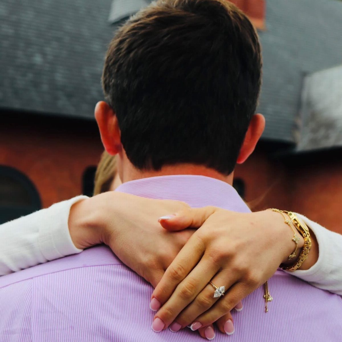 Woman's hands with a diamond engagement ring wrapped around a man's neck.