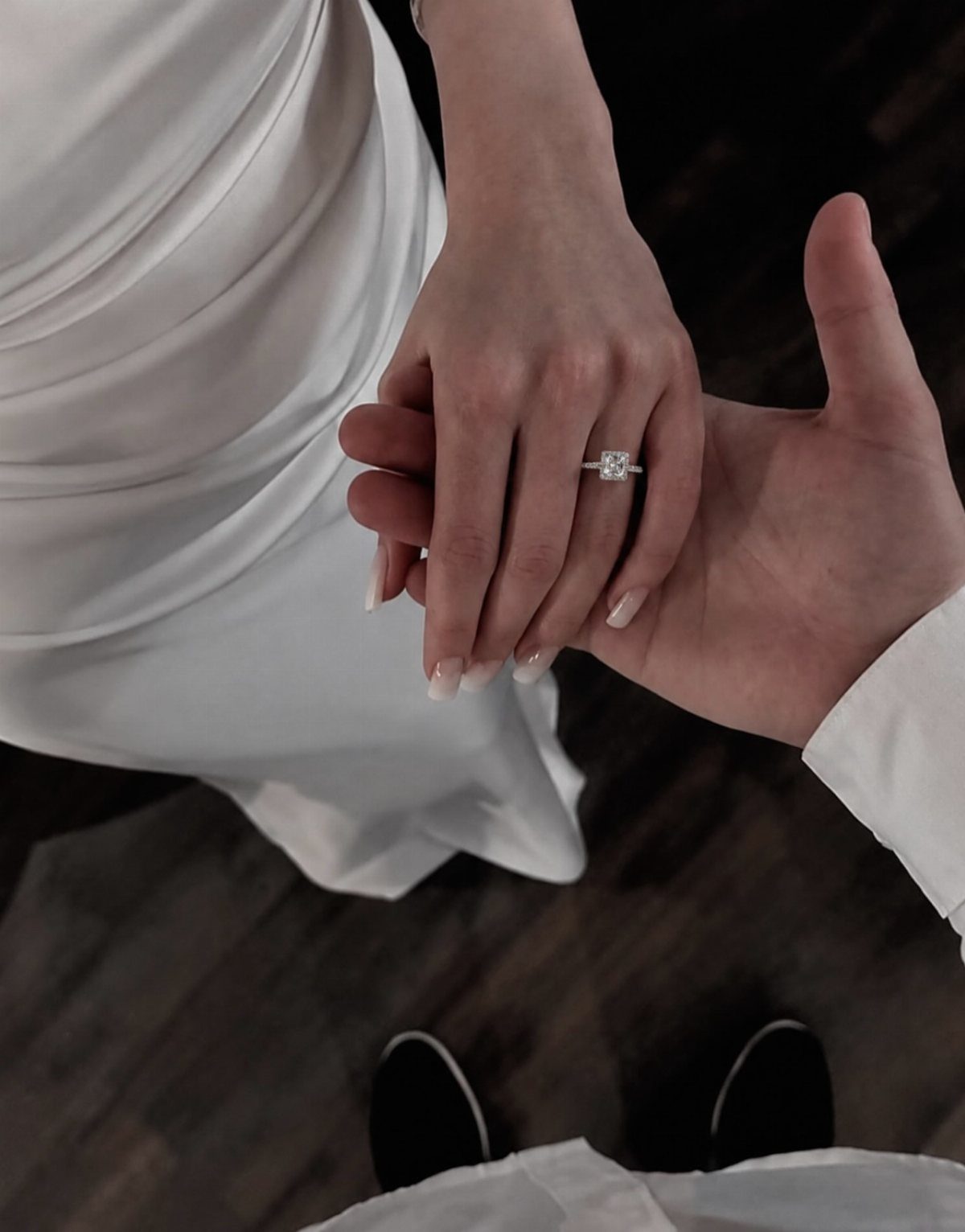 Couple holding hands with a diamond engagement ring visible on the woman's finger.