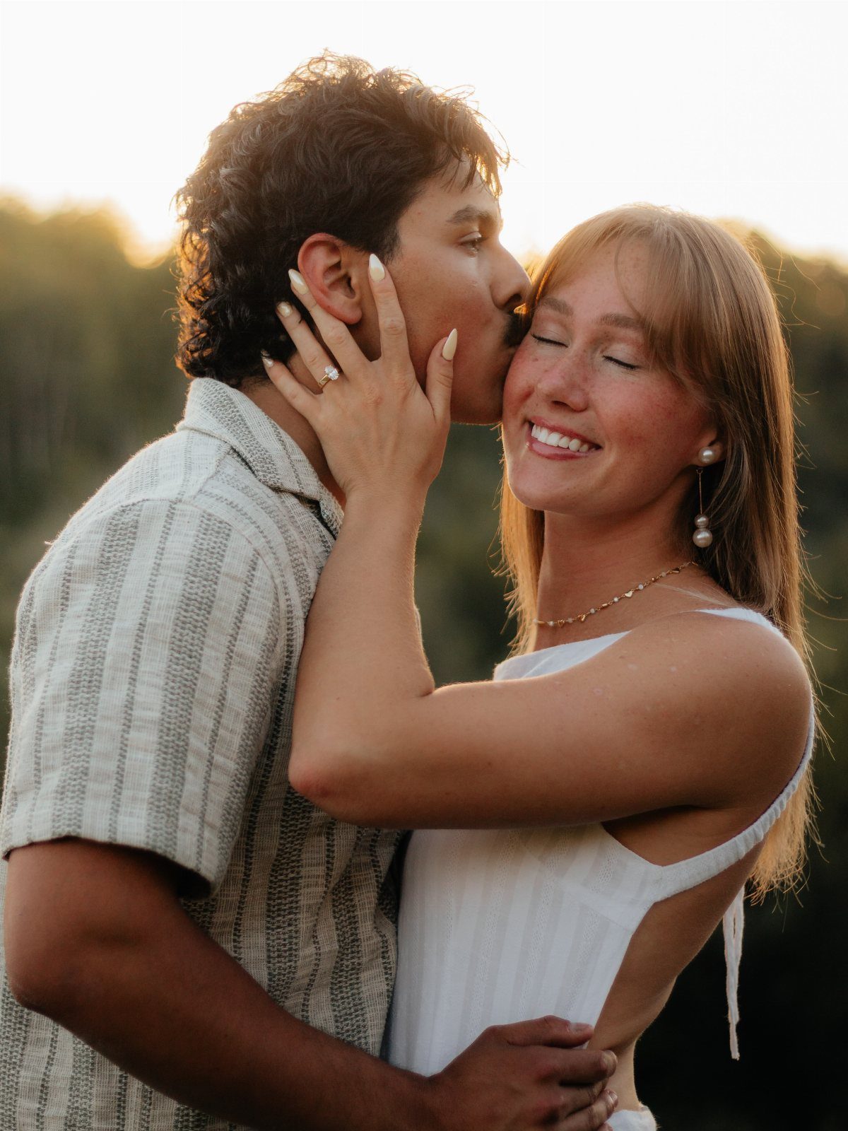 Couple embracing at sunset with a diamond ring visible on the woman's hand.